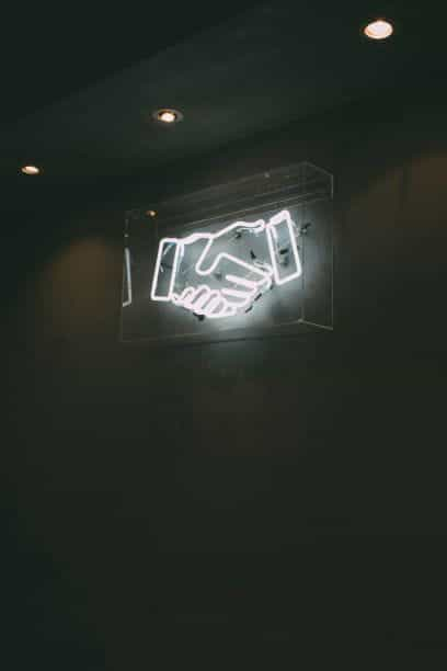 A white neon sign showing a handshake.