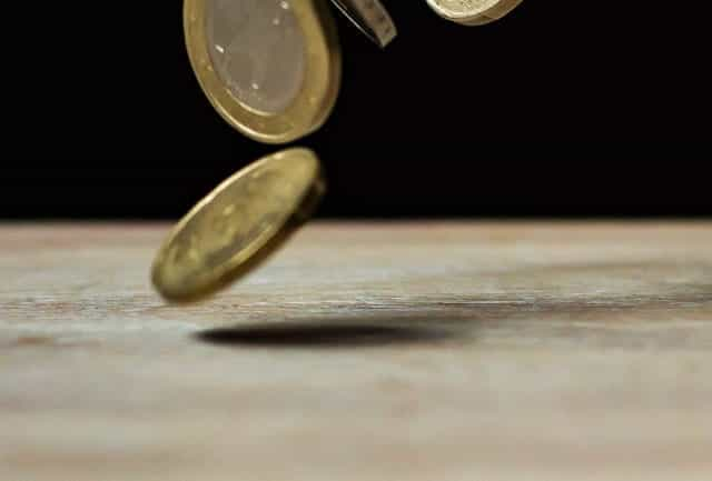 Euro coins fall onto a wooden tabletop.