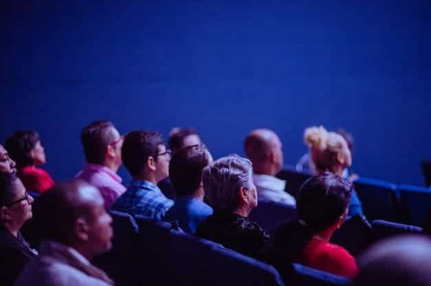 A crowd sits and watches in a theater space.