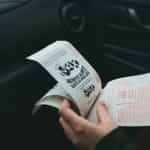 A hand holds lottery tickets, while seated in a car.