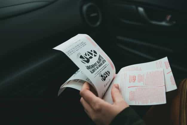 A hand holds lottery tickets, while seated in a car.