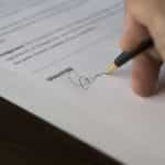 A hand signing a document with a pen.