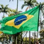 The Brazilian national flag waves in front of palm trees.