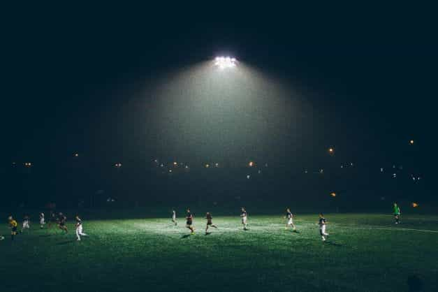 A group of football players playing under floodlights.