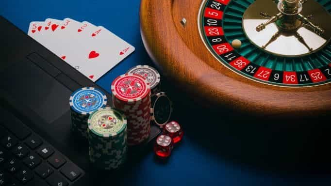 Poker chips, playing cards and a roulette wheel placed close to a laptop.