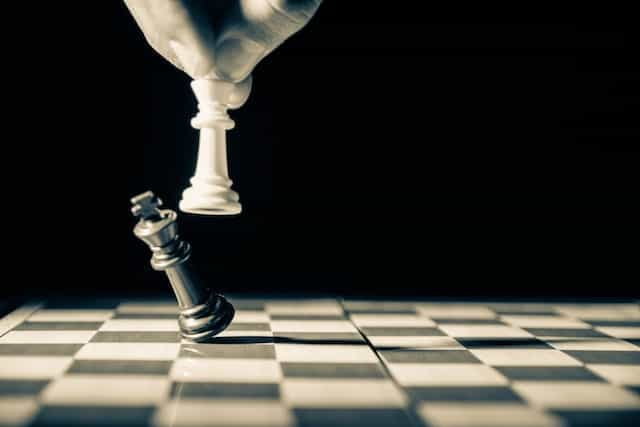 A hand holding a white chess piece knocks over a black chess piece to win the game.