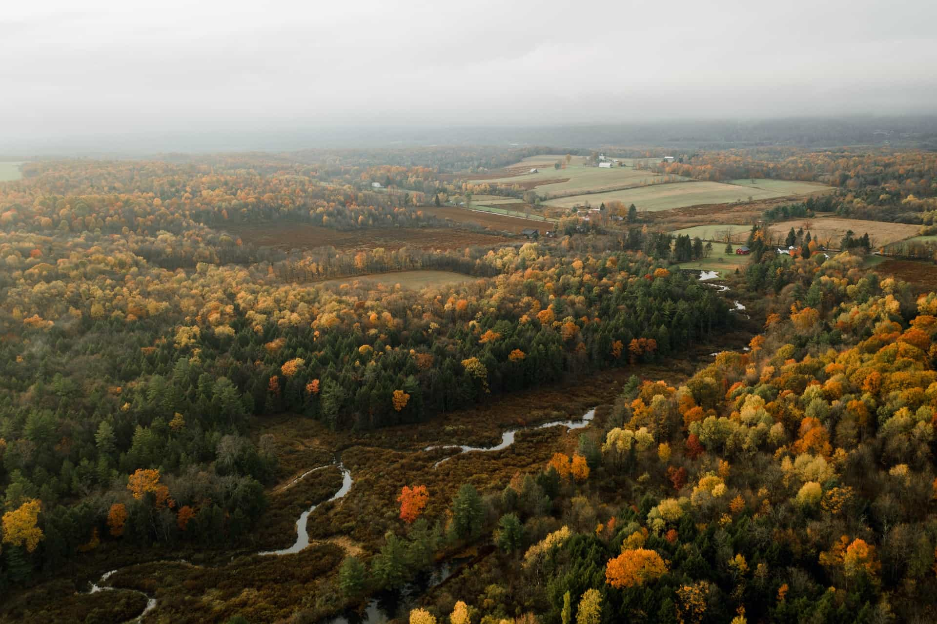 An aerial view of a rural landscape in the US state of Pennsylvania during the autumn season, featuring wide-reaching forests, a small river, and farmland.