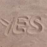 The word “yes” drawn into the sand on a beach or in a desert.