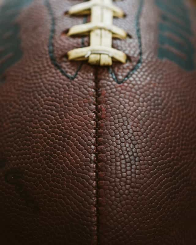 A very close up shot of an American football, featuring its iconic ridge and pigskin brown texture.