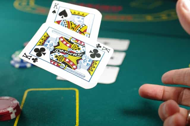 A person throwing a pair of kings during a card game at a casino table.