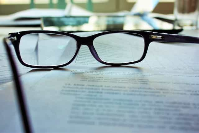 A pair of glasses resting atop a pile of paperwork placed on a table.