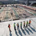 Seven workers or surveyors in high-vis and protective gear standing in a construction site and assessing the project’s progress.