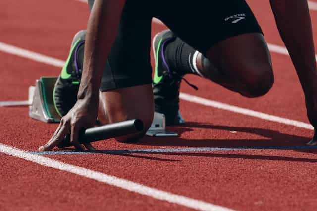 A runner in the ready position at the start line of an outdoor track and field racetrack.